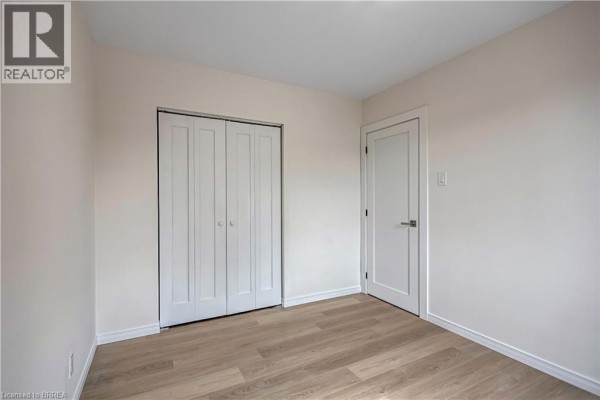A large, empty room with light wood laminate flooring and a wide window overlooking houses and trees. - 1887-1889 Wavell Street, London