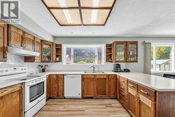 U-shaped kitchen with honey-toned wood cabinets, white countertops, a white stove, and a large window view. - 1888 Nicolls Road, Merritt