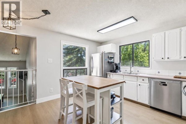 Kitchen with white cabinets, stainless steel appliances, and a central island with two stools. - 189 Deerfield Terrace Se, Calgary