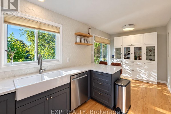 Bright kitchen with a farmhouse sink, white quartz counters, stainless steel dishwasher, and white upper cabinets. - 189 Dunbarton Court, Ottawa