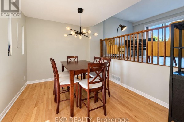 Dining area with a wooden table set for six, a modern chandelier, and light wood floors. - 189 Dunbarton Court, Ottawa
