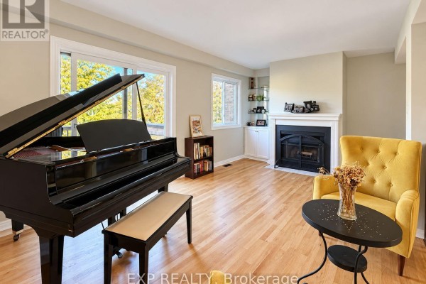 Living room featuring a grand piano, yellow accent chair, fireplace, and large windows. - 189 Dunbarton Court, Ottawa