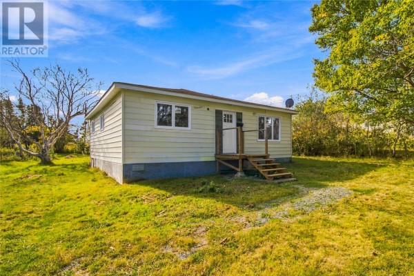 Side view of a light yellow single-story house with a green lawn and trees. - 189 Quigleys Line, Bell Island