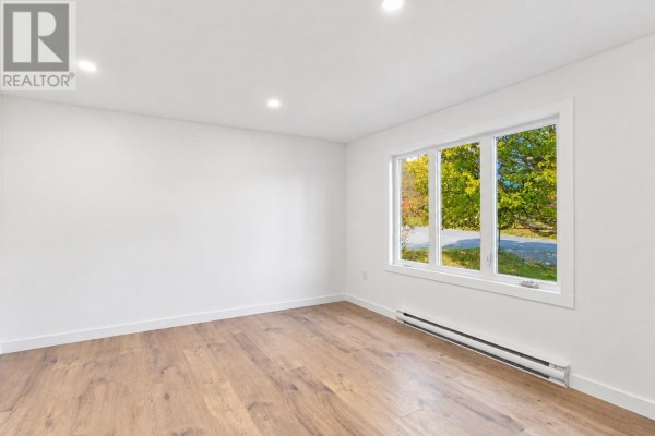 Empty room with white walls, recessed lighting, and a large window with a view of trees. - 189 Quigleys Line, Bell Island