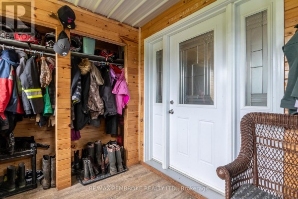 Covered porch with wood paneling, a white front door, and a storage closet filled with coats and boots. - 1890 Queensline Road, Whitewater Region