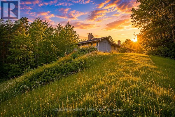 A house sits on a grassy hill under a colorful sunset sky with trees in the background. - 18954 The Gore Road, Caledon