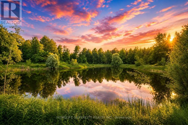 A serene pond reflects the trees and a colorful sunset sky, surrounded by green foliage. - 18954 The Gore Road, Caledon