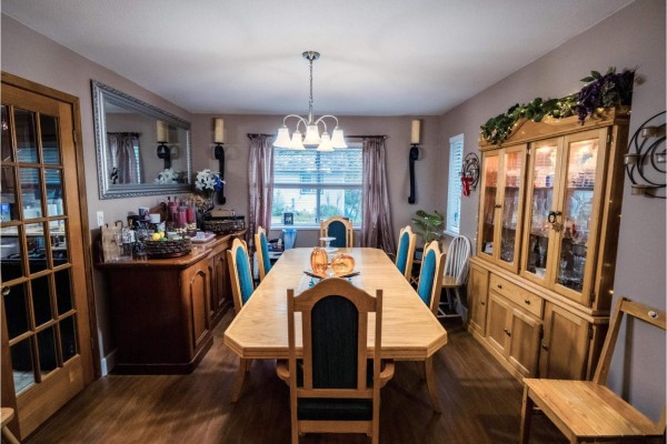 Dining room with a long wooden table, blue chairs, and a china cabinet, illuminated by a chandelier. - 18961 60b Avenue, Surrey