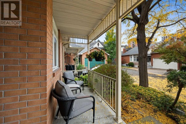 Covered front porch with two chairs and a small table, overlooking a tree-lined yard. - 19 - 1240 Kilborn Place, Ottawa