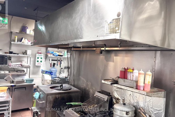 Commercial kitchen with stainless steel ventilation hood, fryers, and condiment bottles. - 19 - 4585 Highway 7 Road W, Vaughan
