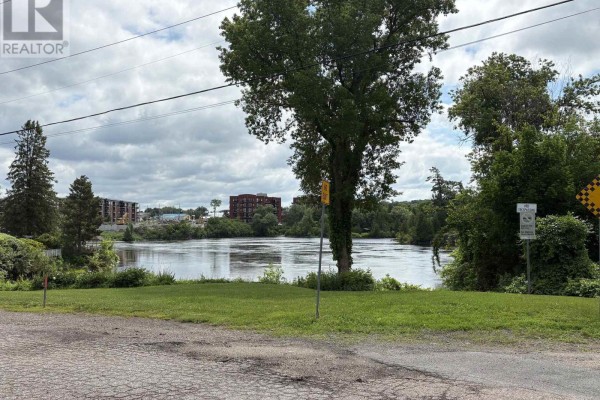 Wide view of a calm river with green trees on the banks and buildings in the distance. - 19 & 21 Rock Lane E, Arnprior
