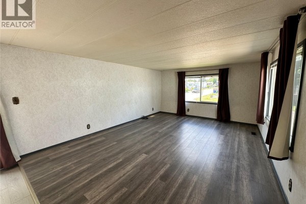 Spacious living room with wood-look flooring, large windows, and white textured walls. - 19 1035 Boychuk Drive, Saskatoon