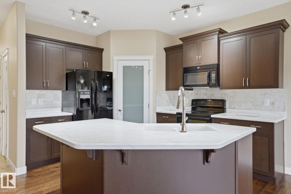 Kitchen featuring dark wood cabinets, black appliances, a white island with a marble countertop, and subway tile backsplash. - #19 340 Spruce Ridge Rd, Spruce Grove