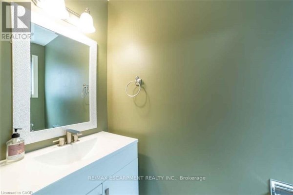 A bathroom vanity with a white sink, silver faucet, and a decorative mirror with green walls. - 19 Beachgrove Crescent, Hamilton