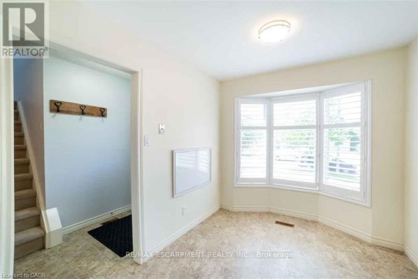 A room with a bay window, beige walls, and a view of the exterior, adjacent to the hallway. - 19 Beachgrove Crescent, Hamilton
