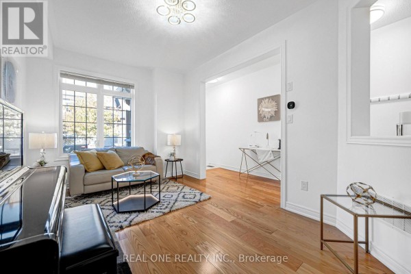 Living room with a beige sofa, coffee table, geometric rug, and a large window with autumn foliage view. - 19 Begonia Street, Markham