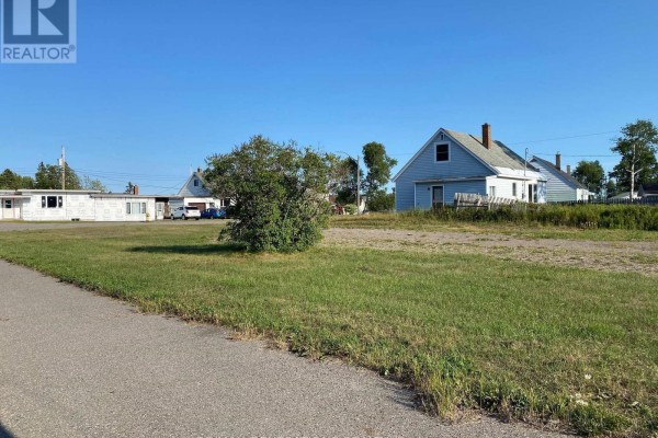 View of an empty lot with grass, gravel, a bush, and houses. - 19 Birch Crescent, Terrace Bay
