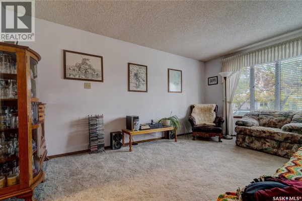 Living room featuring a plush carpet, large window with sheer curtains, and floral patterned sofa. - 19 Cavendish Street, Regina