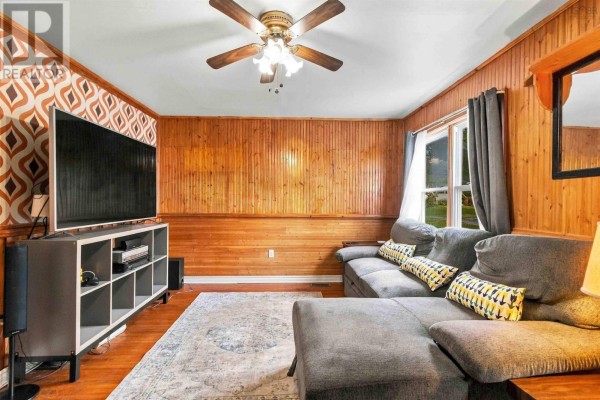 Living room with wood paneled walls, a grey sectional sofa, and a large television. - 19 Central Boulevard, Liverpool
