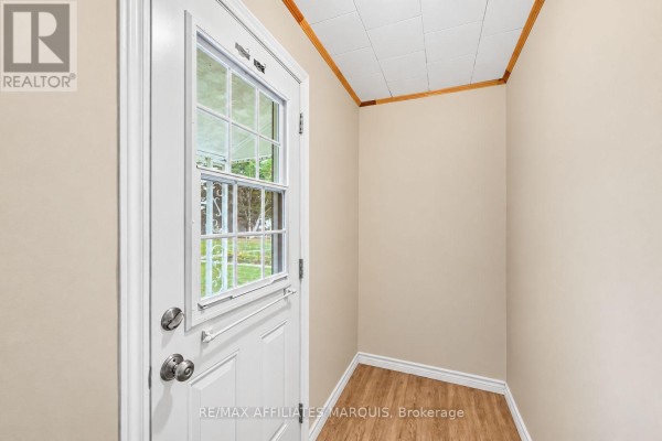 Interior view of a small entryway with a white door, beige walls, and wood-look floor. - 19 Churchill Crescent, Smiths Falls