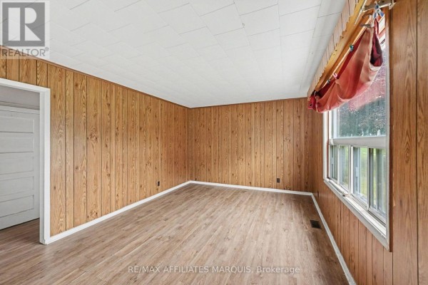 Living room with wood paneled walls, a large window, and light wood-look flooring. - 19 Churchill Crescent, Smiths Falls