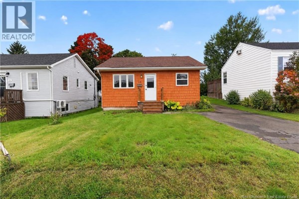 Side exterior of orange wood-shingled bungalow with green lawn and driveway. - 19 Copp Street, Dieppe