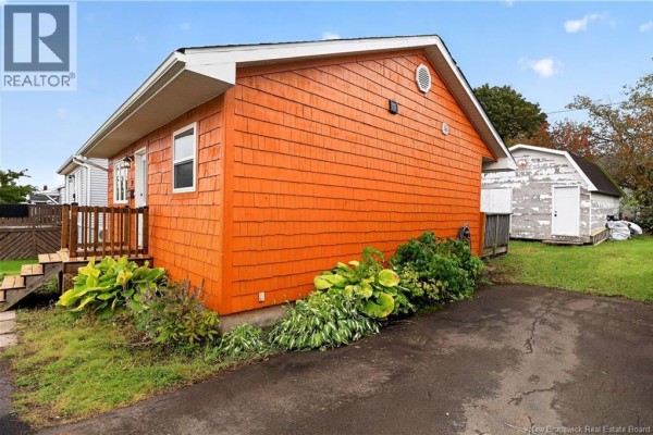 Right side exterior of orange wood-shingled bungalow with green lawn and shed. - 19 Copp Street, Dieppe