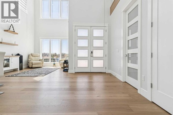 Spacious entryway with tall ceilings, white walls, and a glass-paneled double front door. - 19 Duhram Way, Rural Rocky View County