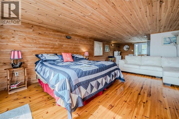 Bedroom with a large quilt-covered bed, wood-paneled walls and ceiling, and a white sectional sofa. - 19 Eagle Road, Tobermory