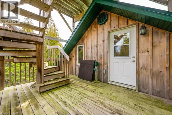 Exterior view of a wood-sided building with a green metal roof and a wooden spiral staircase on a deck. - 19 Eagle Road, Tobermory