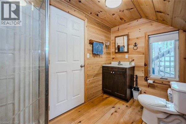 Bathroom with a glass shower stall, dark wood vanity, toilet, and knotty pine walls and flooring. - 19 Eagle Road, Tobermory