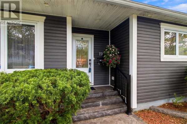 Close-up of the entrance to a dark grey siding bungalow with stone steps and a hanging flower basket. - 19 First Avenue, St  John S