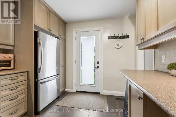 Kitchen entrance area with stainless steel refrigerator, light wood cabinets, and frosted glass door. - 19 Flempton Crescent, Toronto