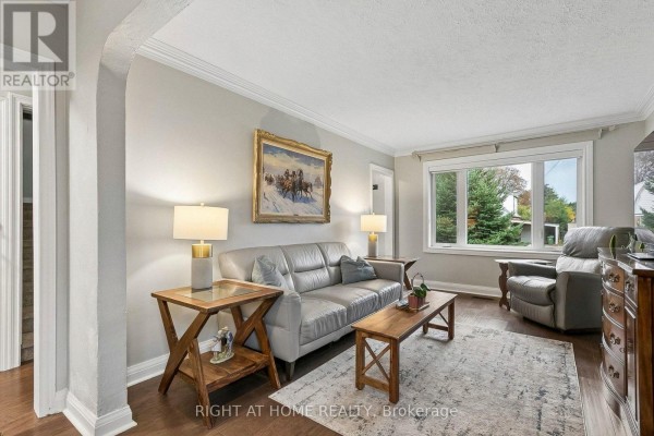 Living room with leather sofa, armchair, wooden furniture, and windows overlooking greenery. - 19 Flempton Crescent, Toronto