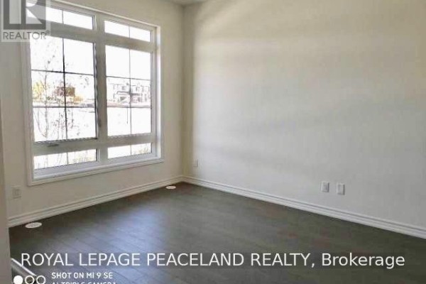 Empty room with light wood floors and a large window with a view of houses. - 19 Frank Charlton Avenue, Markham
