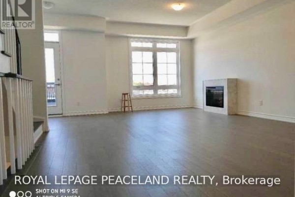 Living area with light wood floors, fireplace, and large window overlooking outdoor space. - 19 Frank Charlton Avenue, Markham