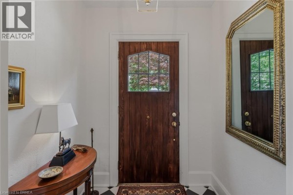 Foyer with a dark wood door featuring a glass pane and a gold-framed mirror on the wall. - 19 Inwood Drive, Brantford