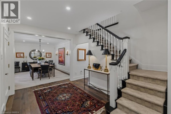 View of the foyer and staircase, opening to a dining room with a large wooden table. - 19 Inwood Drive, Brantford