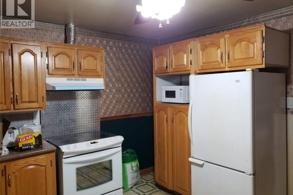 A kitchen with oak cabinets, white appliances, and patterned wallpaper. - 19 John Street, Miramichi