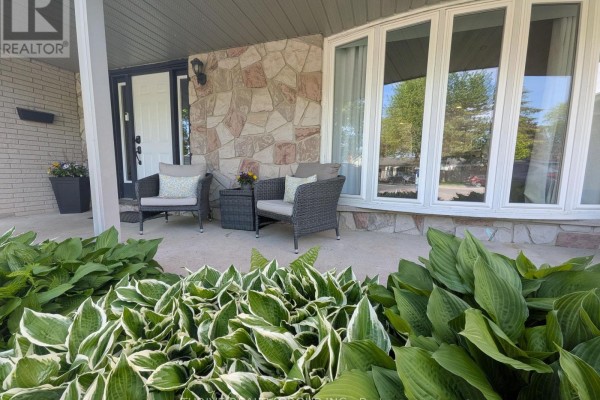 Close-up of a covered front porch with two chairs, a small table, and hosta plants. - 19 Kendall Court, London North