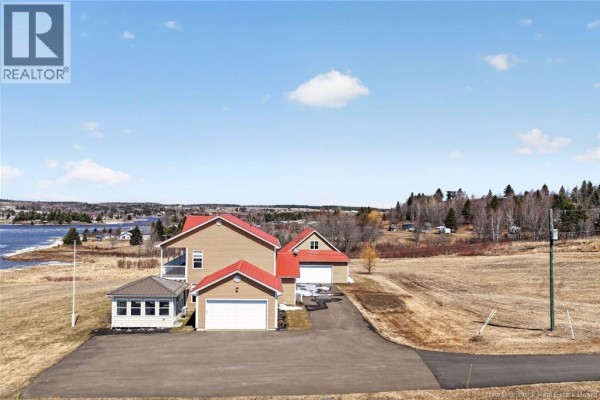Side view of a tan house with a red roof, featuring two garage doors, a sunroom, and a balcony, set against a rural landscape. - 19 Leopold Goguen Road, Sainte Marie De Kent