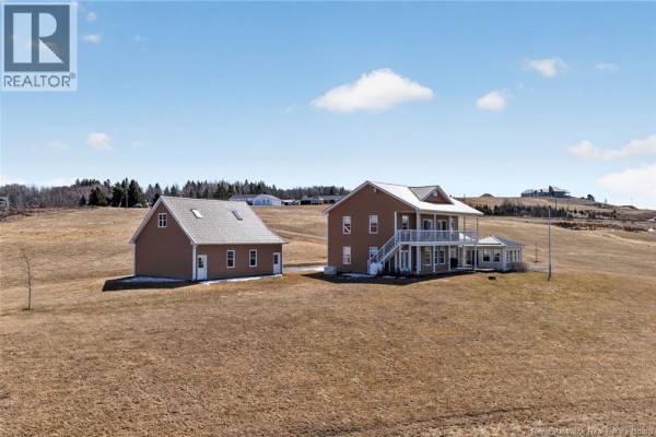 Wide shot of a tan house and detached garage on a dry, grassy field under a blue sky with scattered clouds. - 19 Leopold Goguen Road, Sainte Marie De Kent