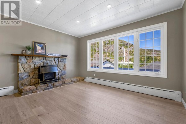 Living room fireplace made of stone with a gas insert, facing a large window with a view of houses and hills. - 19 Long Run Road, Petty Harbor   Maddox Cove