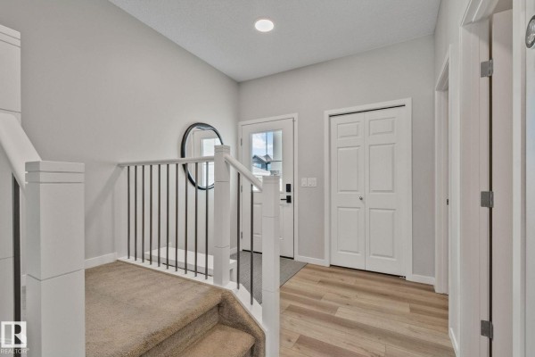 Foyer with carpeted stairs, a railing, a round mirror, and wood-look flooring. - 19 Meadowbrook Wy, Spruce Grove