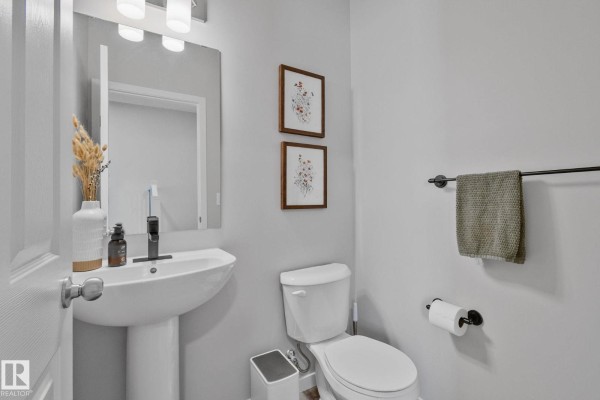 Powder room with a white pedestal sink, toilet, mirror, and framed botanical prints. - 19 Meadowbrook Wy, Spruce Grove