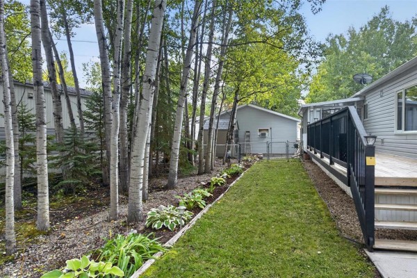 Backyard view of a mobile home with a wooden deck and mature trees lining the property. - 19 Nature Drive, Ste Anne Rm