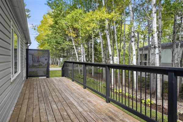 Another view of the wooden deck and backyard, showing the mobile home's exterior siding and windows. - 19 Nature Drive, Ste Anne Rm