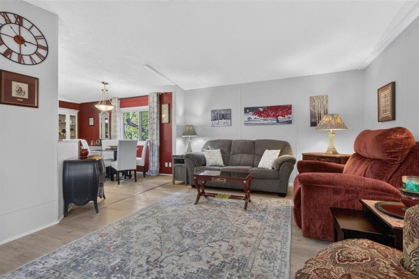 Living room with a grey sofa, recliner, coffee table, and patterned rug. Dining area visible in background. - 19 Nature Drive, Ste Anne Rm