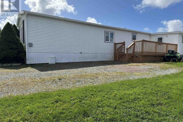 Rear view of the white mobile home showing a wooden deck and green grass. - 19 Old Wharf Road, Havre Boucher