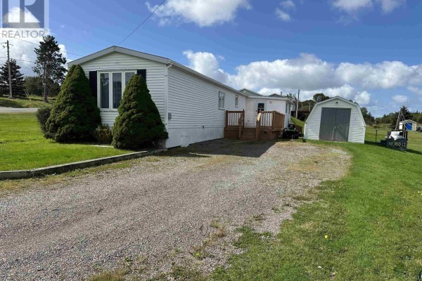 Side view of the white mobile home with a wooden deck, shed, and gravel driveway. - 19 Old Wharf Road, Havre Boucher